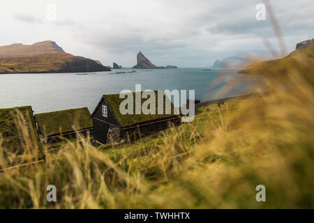 Grass-covered picturesque houses at the Faroese coastline in the village Bour with view onto Dranganir and Tindholmur during spring (Faroe Islands) Stock Photo