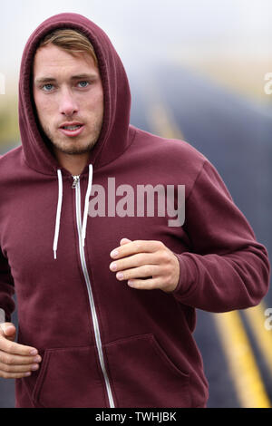 Runner athlete man running training on road in fall in sweatshirt hoodie in autumn. Male runner training outdoors jogging in nature.