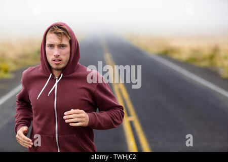 Athlete man running training on road in fall in sweatshirt hoodie in autumn. Male runner training outdoors jogging in nature. Stock Photo