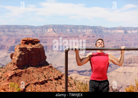 Fitness athlete man training pull ups in amazing nature landscape of Grand Canyon. Strength training fit male working out exercising outdoors in summer doing pull-ups and chin-ups. Stock Photo