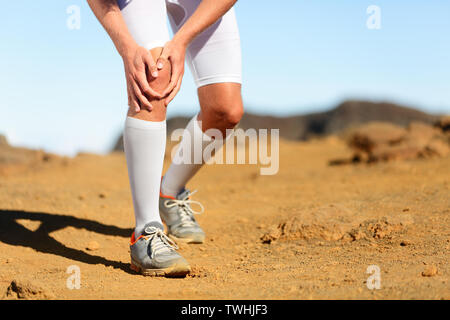 Running injury - Male runner with knee pain. Trail runner injured jogging in nature clutching his knee in pain. Man fitness athlete. Stock Photo