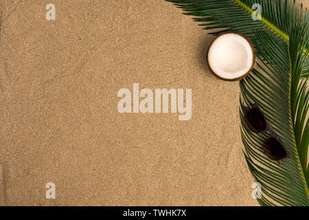 Beach theme on the sand background. Palm leaves, coconut, sunglasses on the sand. Top view. Stock Photo
