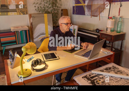 Middle aged man using computer in his art studio and drawing on his tablet Stock Photo