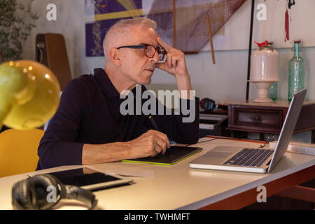 Middle aged man using computer in his art studio and drawing on his tablet Stock Photo