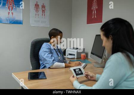 Doctor working on computer while woman looking at ultrasound scan Stock Photo