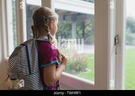 Cute girl with school bag looking outside through window in a comfortable home Stock Photo