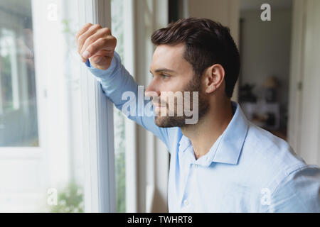 Thoughtful man looking outside through window in a comfortable home Stock Photo