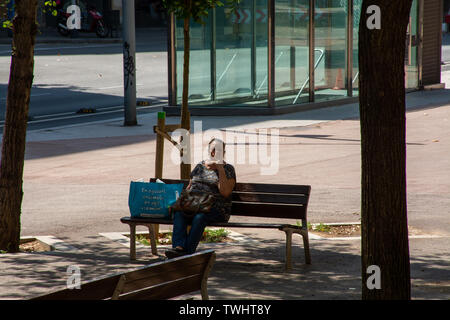 Barcelona, Spain - 27th July 2017 - Old lady with cigarette sitting on a bench in Barcelona Spain Stock Photo