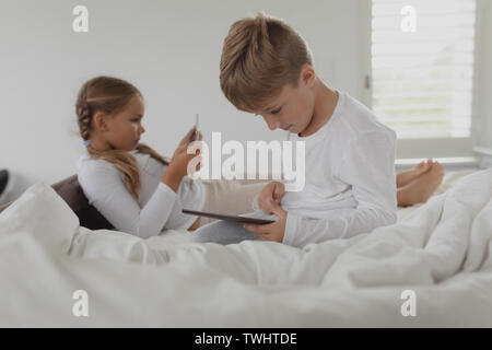 Siblings using digital tablet on bed in bedroom at comfortable home Stock Photo