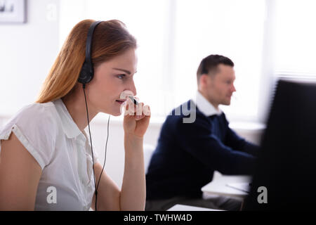 Side View Of Beautiful Female Telephone Operator Talking On Headphones At Workplace Stock Photo