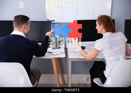 Rear View Of Two Businesspeople Joining Red And Blue Colored Jigsaw Pieces In Office Stock Photo