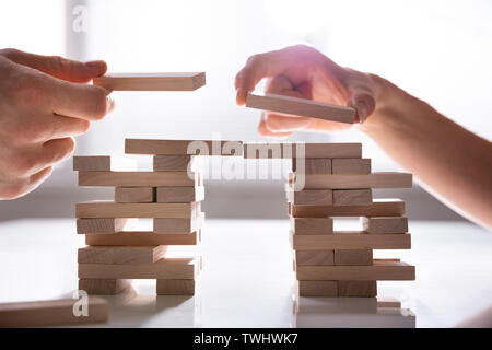 Close-up Of Human's Hand Placing Wooden Block Over Desk Stock Photo