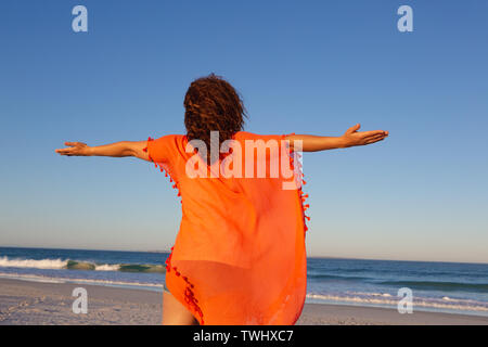 Woman with arms stretched out standing on beach in the sunshine Stock Photo