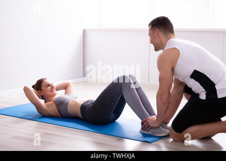 Happy Young Woman Doing Sit Ups With Help Of Trainer At Sport Gym Stock Photo