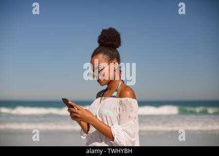 Beautiful woman in sunglasses using mobile phone at beach in the sunshine Stock Photo