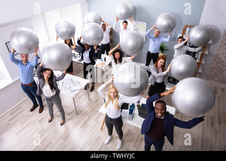 Happy Group Of Businesspeople Stretching Their Arms Using Fitness Ball In Office Stock Photo