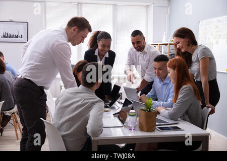 Group Of Young Diverse Business People Working And Communicating While Sitting At The Office Desk Stock Photo