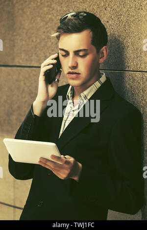 Young handsome business man using tablet computer and calling on cell phone Stylish trendy male model in black suit jacket Stock Photo