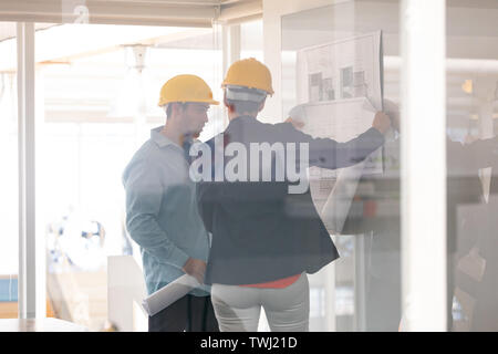 Architects discussing over blueprint on glass board Stock Photo