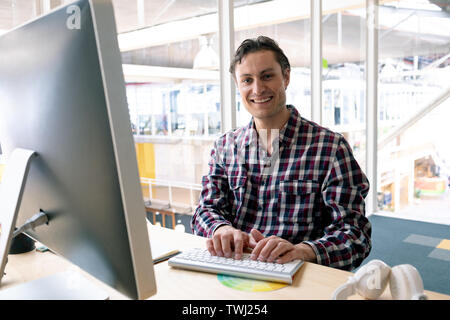 Male graphic designer looking at camera while working on computer at desk in a modern office Stock Photo