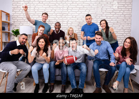 Young Friends Cheering While Watching Rugby Match At Home Stock Photo