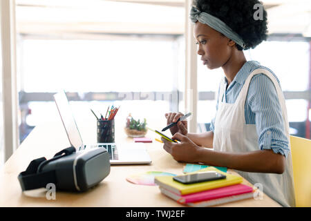 Female graphic designer using graphics tablet while looking at laptop at desk Stock Photo