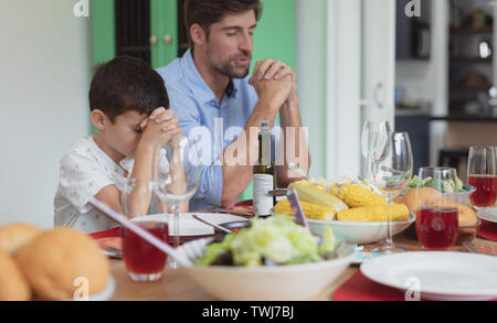 Father and son praying before having lunch at dining table Stock Photo