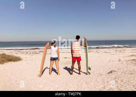 Couple standing with surfboard on beach in the sunshine Stock Photo