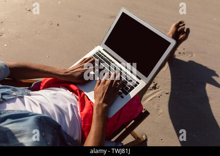 Man using laptop while relaxing in a beach chair on the beach Stock Photo