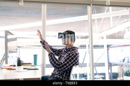 Male graphic designer using virtual reality headset at desk Stock Photo