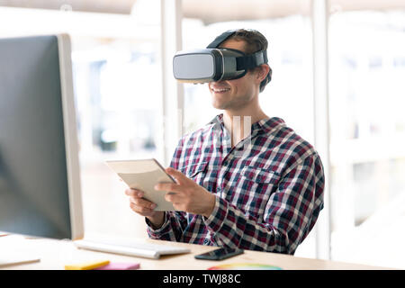 Male graphic designer using virtual reality headset while working on digital tablet at desk Stock Photo