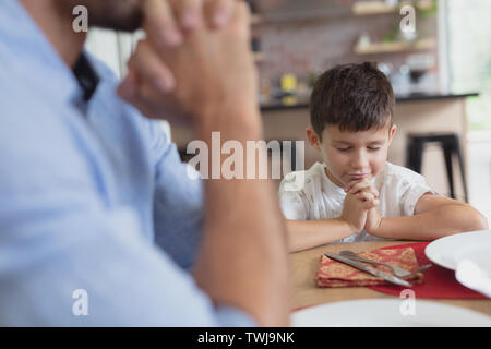 Father and son praying before having lunch at dining table Stock Photo