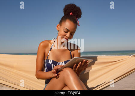 Woman using digital tablet while sitting on hammock at beach in the sunshine Stock Photo