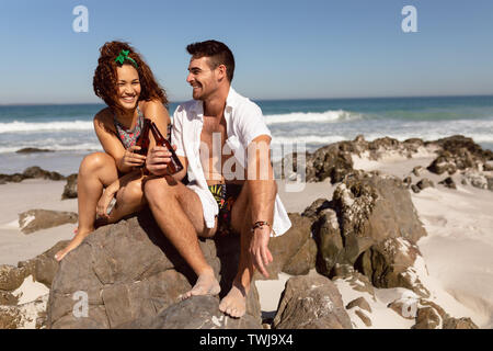 Young couple toasting beer bottle on beach in the sunshine Stock Photo