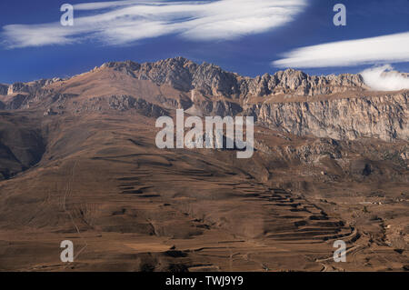 Majestic mountain view - rocky peaks with brownish withered grassy slopes under blue sky with blindingly white clouds Stock Photo