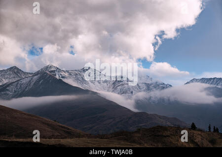 Majestic mountain view - rocky peaks covered with snow on the horizon with some dark brown autumn hills in front under the menacing cloudy sky Stock Photo