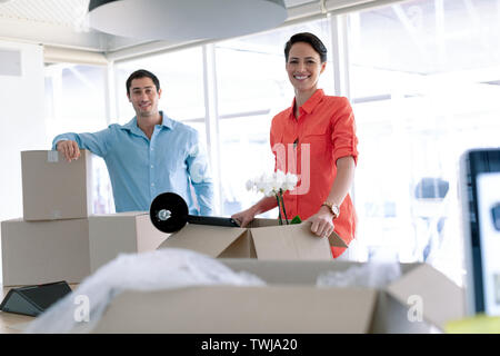 Business people looking at camera while unpacking office belongings from cardboard boxes on table Stock Photo