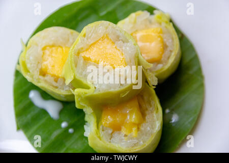 Mango sticky rice with coconut milk roll on banana leaf Stock Photo