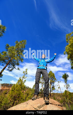 Hiking man reaching summit top cheering celebrating on mountain top with arms up outstretched towards the sky. Happy male hiker. Stock Photo