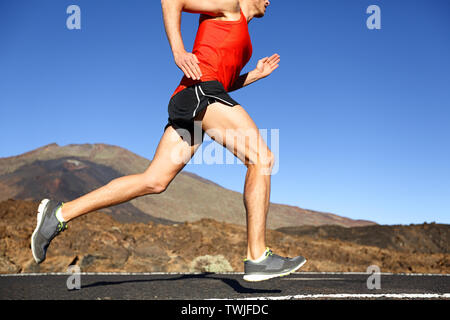 Running man - male runner training outdoors sprinting on mountain road in amazing landscape nature. Close up of fit handsome jogger working out for marathon outside in summer. Stock Photo