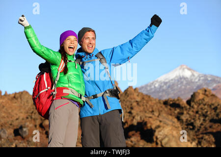 Happy celebrating winning hiking people at top. Cheering hiker couple enjoying freedom on hike with arms raised in mountain landscape. Woman and man on volcano Teide, Tenerife, Canary Islands, Spain Stock Photo
