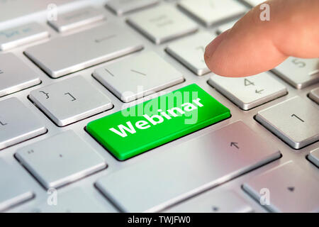 Keyboard with green key Enter and word Webinar button modern pc text communication board. Color button on the gray silver keyboard of modern ultrabook Stock Photo