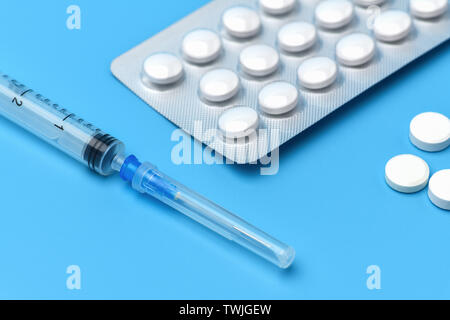 Many tablets are on a blue background, at the bottom is a syringe with an injection. Drugs and pills prescription background. Pharmaceutical preparati Stock Photo