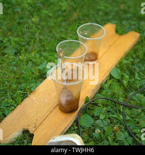 Three empty plastic glasses with spoon placed on the grass, outdoor close-up Stock Photo