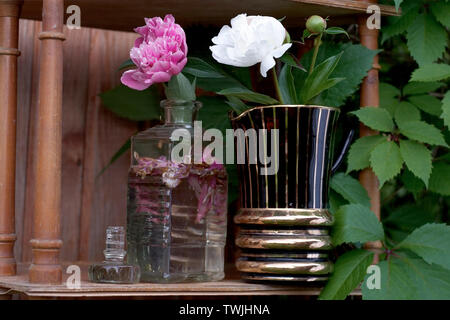 Beautiful pink and white peonies in vases placed on the wooden bookcase, outdoor close-up Stock Photo