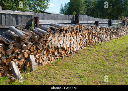 Chopped firewood stacked in a woodpile near the fence in the village Stock Photo