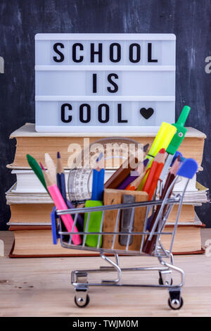 Set of colored pencils and markers for school in shopping cart. Lettering School is cool on a pile of books Stock Photo