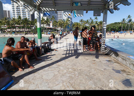 Local people and visitors hang around at ease on the Waikiki Wall which decides Kuhio Beach and Queen's Beach at Waikiki, Hawaii. Stock Photo