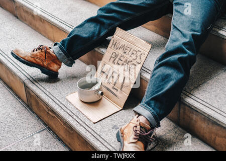 Old homeless person sleeping on stairs with cardboard and text homeless please help with dollar in can Stock Photo