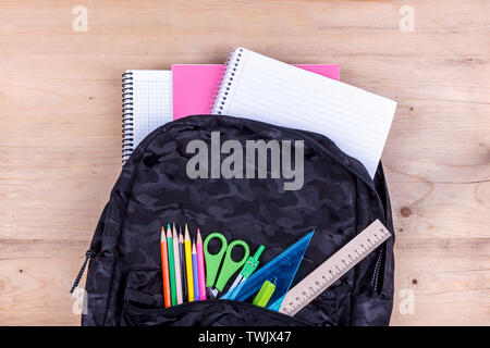 Black school bag with set of stationery for the student and with white notebook in it. Back to school concept Stock Photo